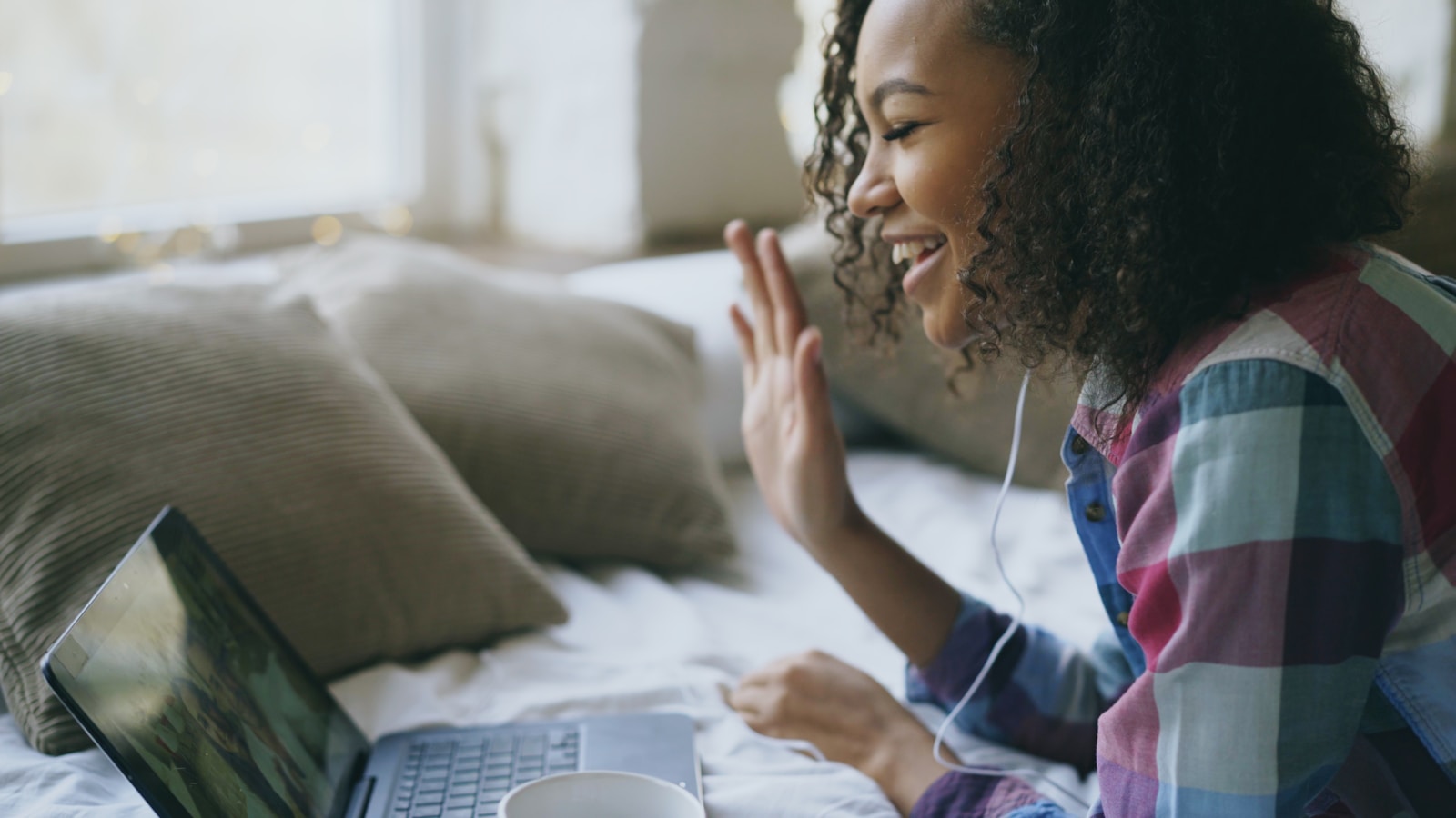 A young woman waves during a video call on laptop.